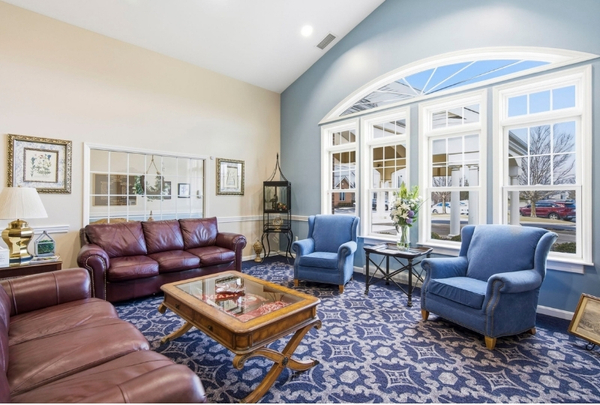 Bright living room with burgundy leather sofa, two blue armchairs, glass coffee table, and a large arched bay window.